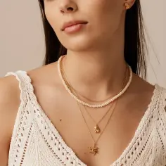 Delikatny choker z białych koralików i złote łańcuszki z zawieszkami. Taka biżuteria podkreśla subtelność i elegancję, pokazując, co oznacza choker na szyi.