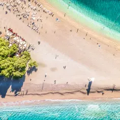 Plaża w Chorwacji z turkusową wodą i zielonymi drzewami. Idealne miejsce, by sprawdzić apartament w Chorwacji i cieszyć się słońcem.