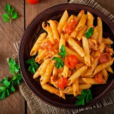 Penne z kurczakiem i pomidorami, udekorowane natką pietruszki. Idealne danie, co można zjeść na obiad.