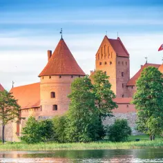 Zamek w Trokach, jedna z głównych atrakcji Litwy, z czerwonymi dachami i wieżami, otoczony zielenią i wodą.