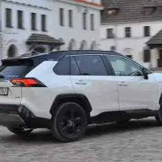 Biała Toyota RAV4 Hybrid, jeden z popularnych modeli hybrydowych, jedzie po brukowanej ulicy.