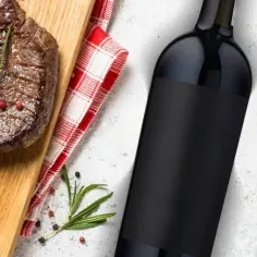 Jak dobrać wino do steka wołowego? Stopień wysmażenia a taniny. Aromatyczny stek wołowy, butelka czerwonego wina, zioła i przyprawy.
