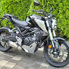 Czarny motocykl Honda z serii CBR, z chromowanym wydechem LeoVince, stoi na kostce brukowej przed żywopłotem.