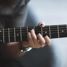 Dłoń z czarnym lakierem na paznokciach gra akord na gitarze. Może to być początek tworzenia alfabetyczny spis piosenek Czerwonych Gitar.