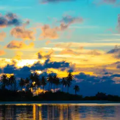 Zachód słońca na Kiribati. Palmy na tle nieba w odcieniach pomarańczy i błękitu. Ciekawe miejsca na wyspach Pacyfiku.