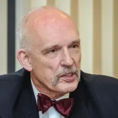 Janusz Korwin-Mikke w garniturze i bordowej muszce, z charakterystycznymi wąsami.