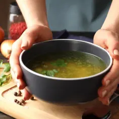 Aromaticzny rosół, jak z przepisu Magdy Gessler, w misce, z dodatkiem ziół i przypraw na drewnianej desce.