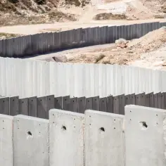 Betonowy mur, symbolizujący podziały i napięcia związane z syjonizmem, wije się po pustynnym krajobrazie.