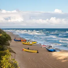Piękna plaża w Rewie i okolicy, z kolorowymi łodziami na piasku i falującym morzem. Idealne miejsce na spacer i podziwianie widoków.