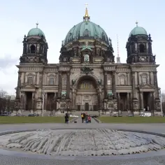 Majestatyczna katedra w Berlinie z zielonymi kopułami, na pierwszym planie kamienna rzeźba.
