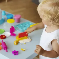 Mała blondynka bawi się masą plastyczną, tworząc fantastyczne zabawy sensoryczne dla 4 latka.