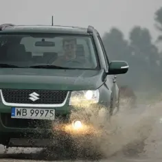 Zielony Suzuki Grand Vitara 1.9 ddis pokonuje kałużę na błotnistej drodze.