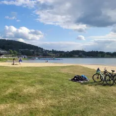 Dwa rowery czekają na plaży nad Jeziorem Rożnowskim. W tle widać ludzi kąpiących się i bawiących w wodzie.