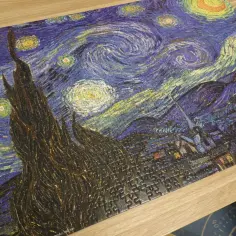 Układanka przedstawia słynny obraz "Gwiaździsta noc" Van Gogha. Wirujące niebo, cyprys i miasteczko nocą.