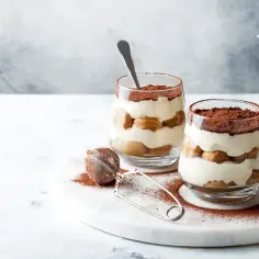 Dwa pucharki z kremowym, warstwowym deserem, posypane kakao. To najprostsze tiramisu, idealne na deser.