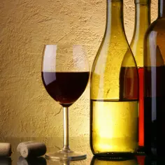Kieliszek czerwonego wina i butelki na tle złotej ściany. Dwa korki leżą obok, sugerując, jak poprawić smak wina.