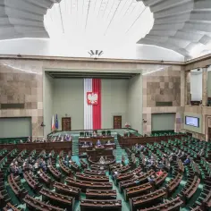 Sala sejmowa z rzędami zielonych foteli, gdzie partie polityczne debatują nad przyszłością kraju.