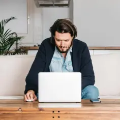 Mężczyzna siedzi na kanapie i pracuje na laptopie.