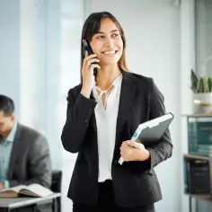 Uśmiechnięta prawniczka rozmawia przez telefon, trzymając teczkę. Jej zawód zaufania publicznego wymaga dyskrecji i profesjonalizmu.