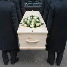 Konduktorzy niosą trumnę ozdobioną białymi różami. Zastanawiasz się, ile zarabia mistrz ceremonii pogrzebowej?