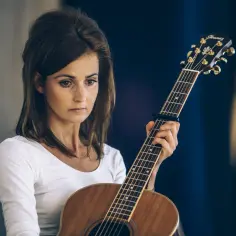 Dominika Żukowska, zamyślona, trzyma gitarę. Jej data urodzenia to tajemnica, którą skrywa w sercu.