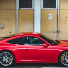 Czerwone Porsche 991 z kierowcą w kasku stoi przed żółtą ścianą z napisem "Zakaz palenia".