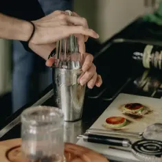 Barman przygotowuje drinka, mieszając w shakerze składniki na wódkę z colą. Na blacie leży butelka whiskey.