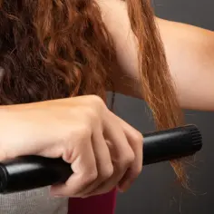 Ruda kobieta prostuje swoje kręcone loki włosy prostownicą.