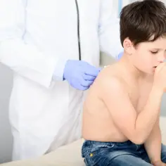 Lekarz w rękawiczkach bada plecy chłopca, który kaszle. Podejrzenie zapalenie płuc u dziecka.