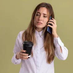 Zmartwiona kobieta z kawą w ręku rozmawia przez telefon, zastanawiając się, dlaczego nikt nie dzwoni po wysłaniu CV. Najczęstsze błędy w dokumentach.