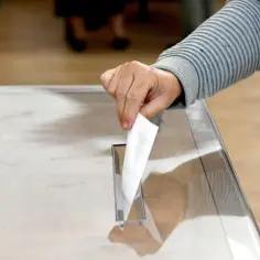Dłoń wrzuca kartę do urny. To symboliczne ucieleśnienie biernego prawa wyborczego, które pozwala obywatelom wpływać na losy państwa.