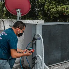 Technik w masce podłącza manometr do jednostki klimatyzacyjnej na dachu.