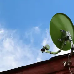 Zielony talerz do satelity zamontowany na drewnianej ścianie, skierowany ku błękitnemu niebu z chmurami.