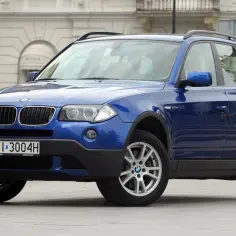 Niebieskie BMW X3 2005 z polskimi tablicami rejestracyjnymi WI 3004H zaparkowane przed budynkiem.