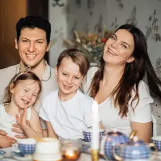 Szczęśliwa rodzina przy stole, dzieci i rodzice uśmiechają się. To obrazek, który może symbolizować radość z życia i wsparcie, jakie daje zasiłek rodzinny.