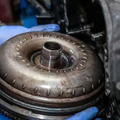 Mechanik w niebieskich rękawiczkach trzyma sprzęgło hydrokinetyczne. Gdy padnie dwumasa, może to oznaczać problemy z płynną jazdą.