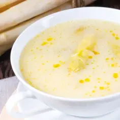 Kremowa zupa szparagowa z kawałkami szparagów i oliwą, obok pęczek białych szparagów.