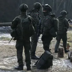Żołnierze w kamuflażu stoją przy torach kolejowych. Zastanawiasz się, ile zarabia szeregowy w wojsku?