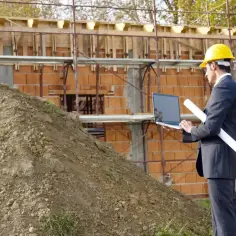 Inżynier w kasku analizuje plany budowy na laptopie, uwzględniając poziom wód podziemnych.