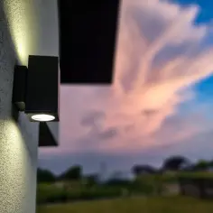 Nowoczesne lampy zewnętrzne na dom oświetlają ścianę, tworząc nastrojowy klimat przy zachodzącym słońcu.