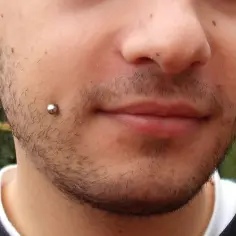 Mężczyzna z kolczykami w policzkach i czarnym tunelem w uchu.