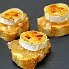 Trzy pinchosy na ciemnym tle: grzanki z dżemem i zapieczonym serem kozim.