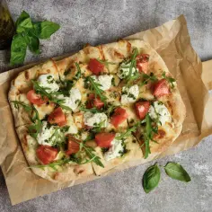 Pyszna pizza bez mięsa z pomidorami, mozzarellą i rukolą, polana zielonym pesto. Idealna dla wegetarian.