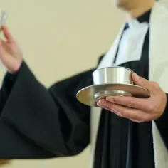Duchowny w komży trzyma kielich i puszkę na hostie. Właśnie trwa komunia, a dzieci zazwyczaj przystępują do niej, gdy mają około 9 lat.