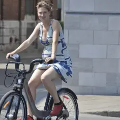 Kobieta w ciąży na rowerze miejskim, w letniej sukience i czerwonych butach. Czy w ciąży można jeździć na rowerze? Tak, jeśli czujesz się dobrze.