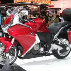Błyszczący, czerwony motocykl Honda VFR 1200 z kuframi, prezentowany na wystawie motoryzacyjnej.