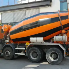 Pomarańczowa betoniarka z czarnymi pasami, zaparkowana na ulicy.