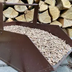 Brązowa łopatka wypełniona pelletem drzewnym na tle stosu drewna.