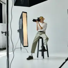Młody fotograf z blond włosami siedzi na stołku w studiu, robiąc zdjęcie. Zastanawiasz się, ile zarabia fotograf?