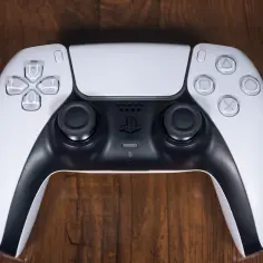 Biały kontroler DualSense do PS5 leży na drewnianym blacie. Zastanawiasz się nad jego ps5 pobór prądu?